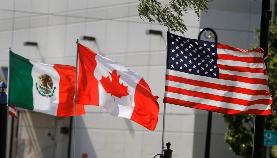 United States flag in the foreground with Canadian and Mexican flags fluttering beside it outside a building in an urban setting.