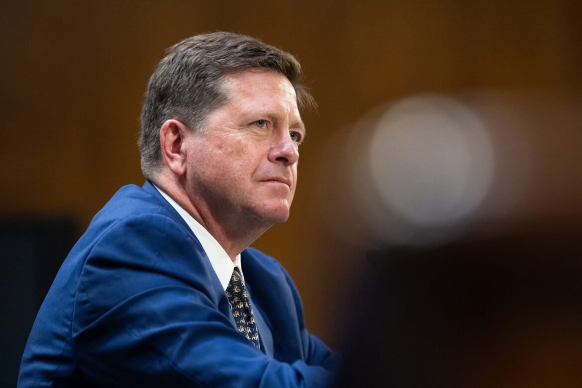 Man in a blue suit in profile, looking to the right in a formal setting.