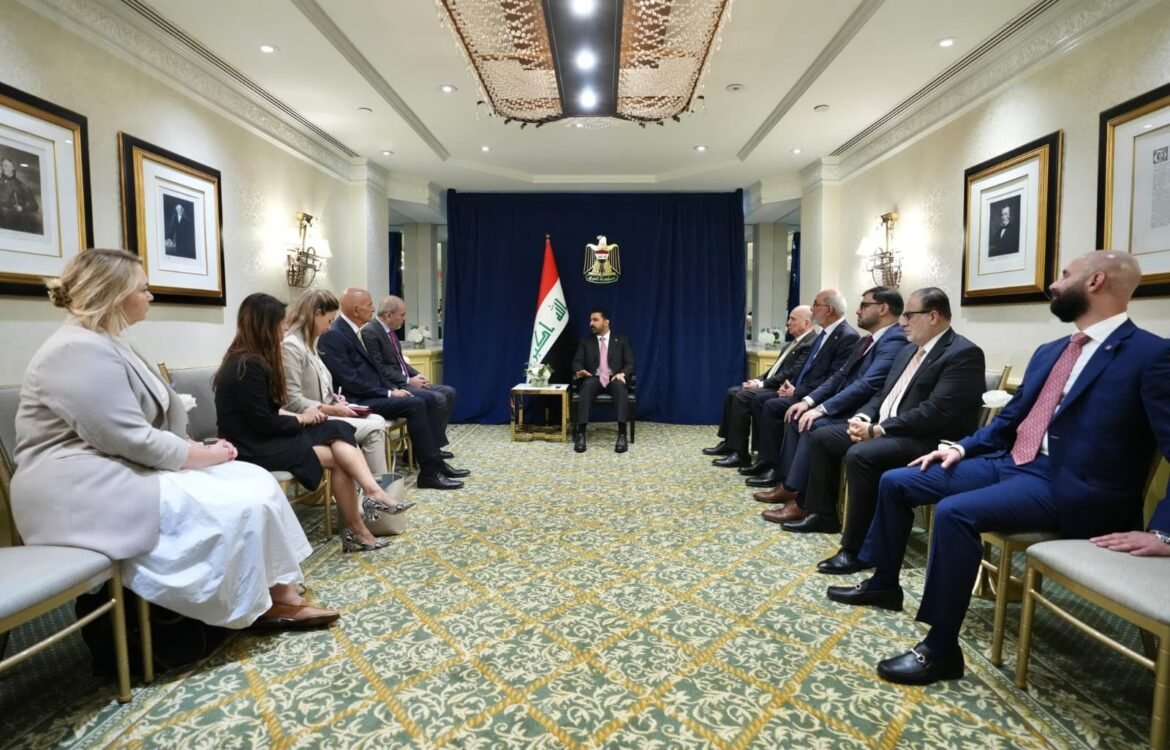 Formal diplomatic meeting in a hotel conference room; officials sit in two rows facing a central speaker with an Iraqi flag and emblem behind them on a blue backdrop.