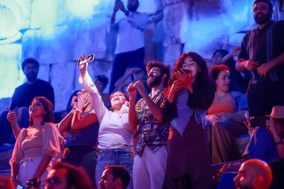 Group of young adults in a blue-lit crowd posing and taking selfies together at an event or concert surface level cheers nearby.
