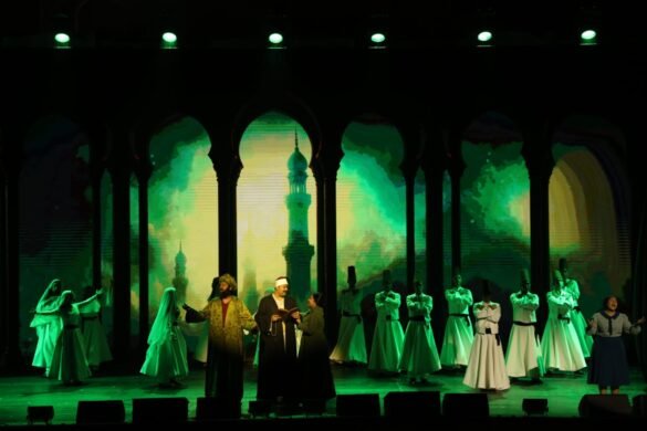 Stage performance with a green-lit backdrop of arches and a central minaret; performers in traditional clothing occupy the center.