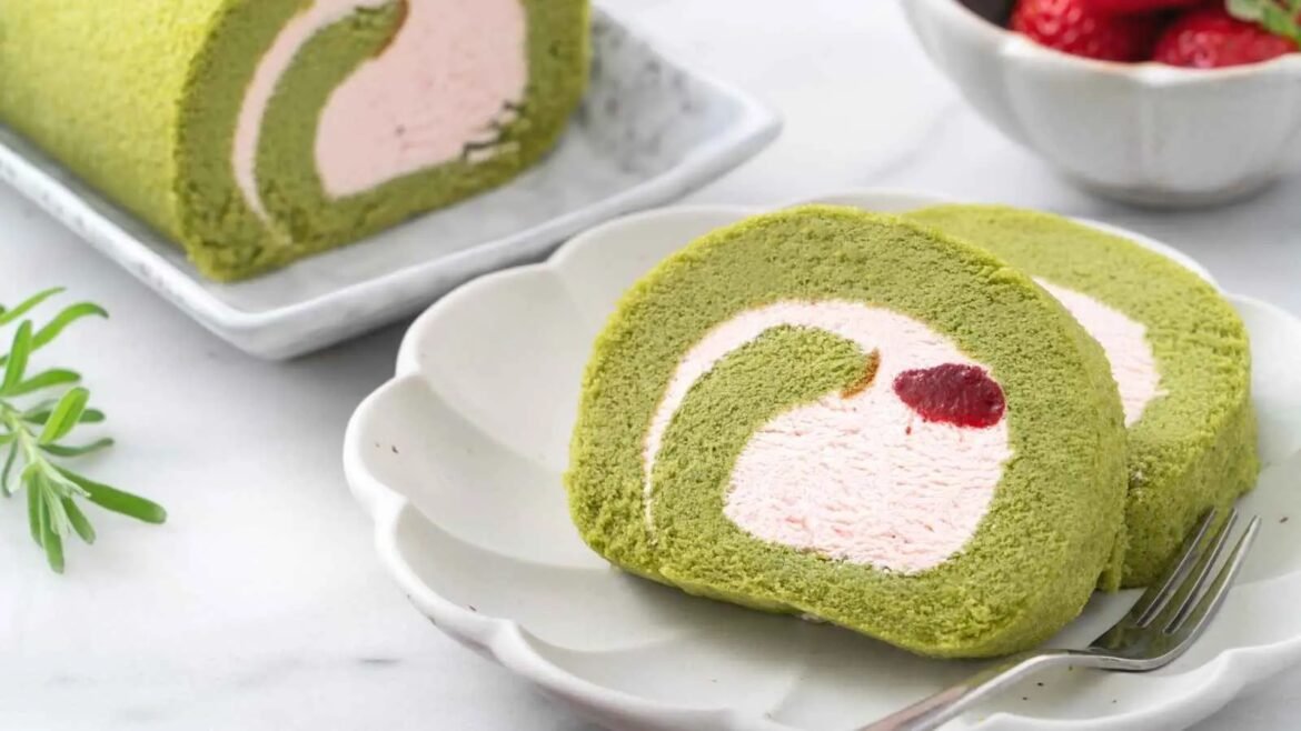 Slice of matcha green tea Swiss roll with pink cream filling and a red berry center on a white plate.