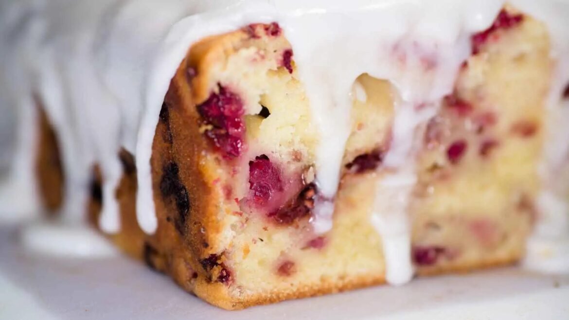 Sliced berry loaf cake with powdered icing glaze dripping down the sides, visible raspberries in the crumb