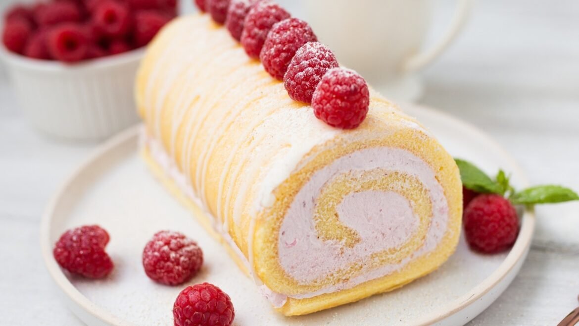 Rolled sponge cake with pink raspberry cream filling, topped with fresh raspberries on a plate.