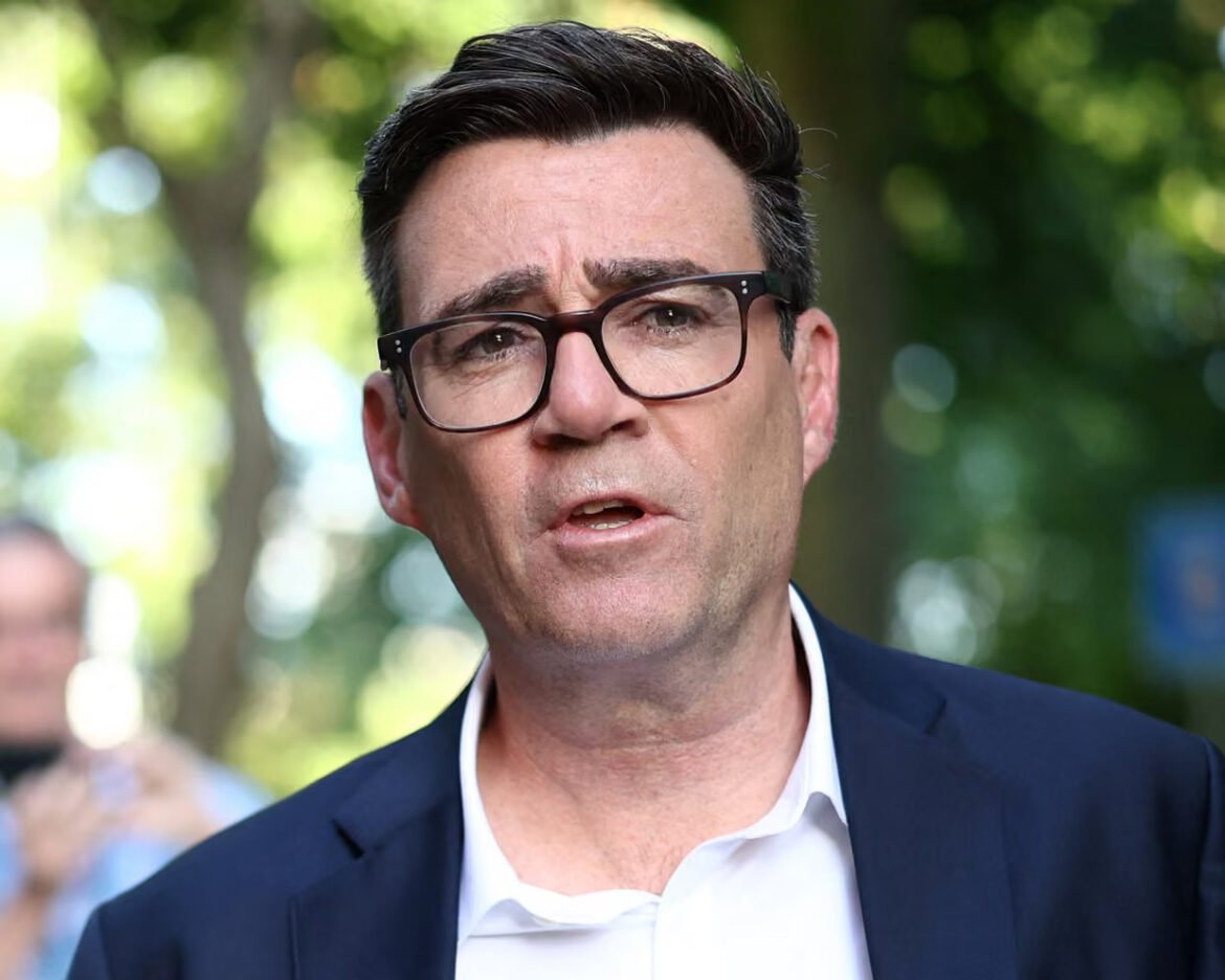 Man with dark hair and glasses in a navy suit speaking outdoors.