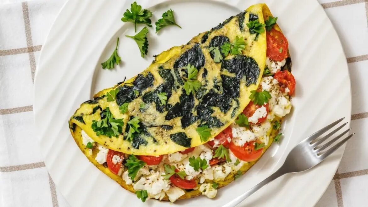 Folded omelette with tomato and feta filling, topped with parsley on a white plate with a fork nearby.