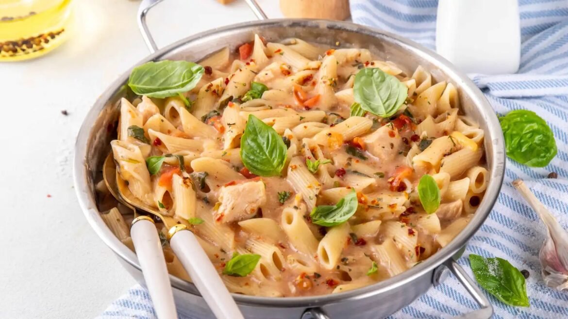 Penne pasta with creamy sauce and chicken, garnished with fresh basil leaves in a skillet
