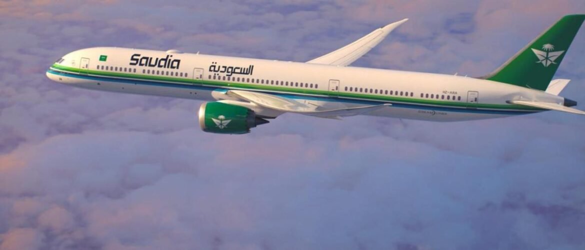 Saudi Arabian Airlines jet in white with green-and-teal livery flying above clouds, mid-flight.