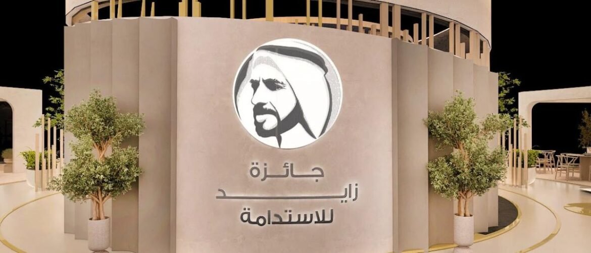 Curved beige wall with a circular Sheikh Zayed logo and the Arabic text جائزة زايد للاستدامة; potted trees nearby.