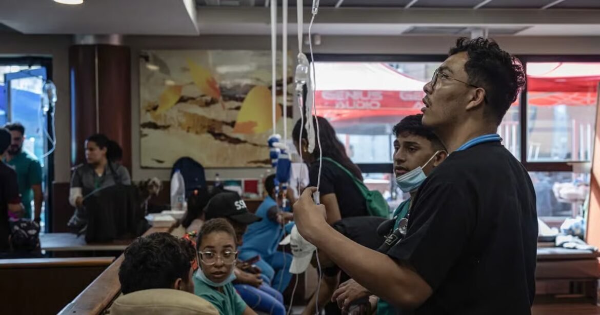 Healthcare workers and patients in a busy clinic; a man in scrubs sets up an IV drip while others wait nearby.