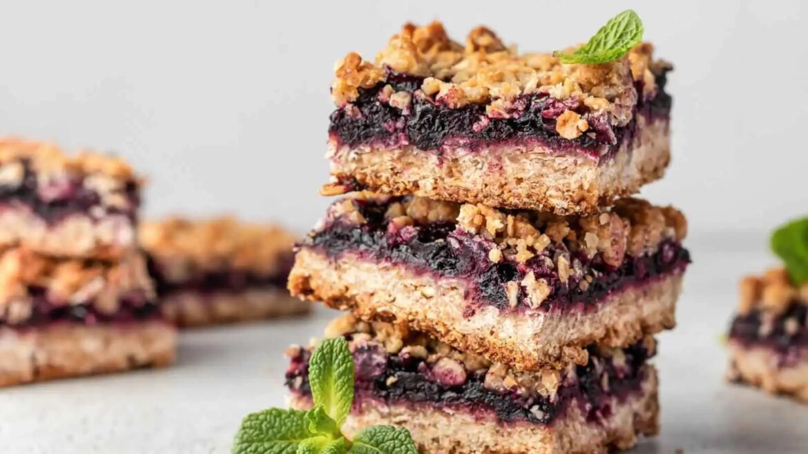 Stack of blueberry crumble bars with oat crust, dark blueberry filling, and streusel topping, garnished with mint leaves