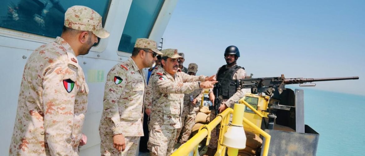 Soldiers in desert camouflage on a ship's deck beside a mounted machine gun, looking toward the water.