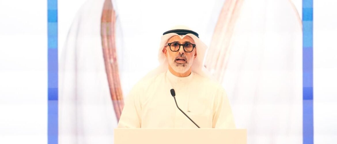 Man wearing a white kandura and ghutra speaks at a podium with a microphone.