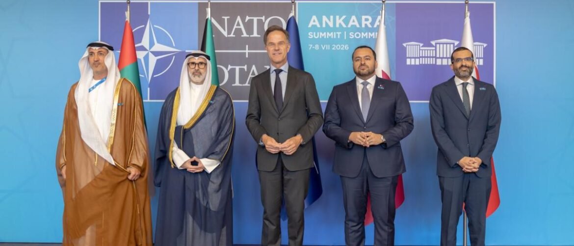 Five men in formal attire stand in a row at a NATO Ankara Summit backdrop with flags behind them for a group photo.