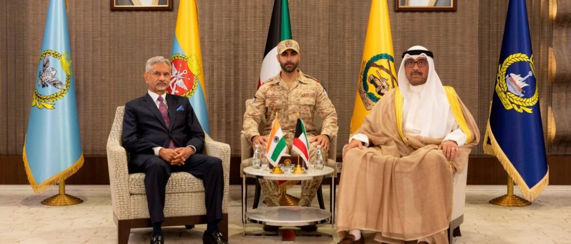 Three men in formal attire seated for a diplomatic meeting; a suited elder on the left, a military officer in the center, and a man in traditional Arab dress on the right, with flags behind them.