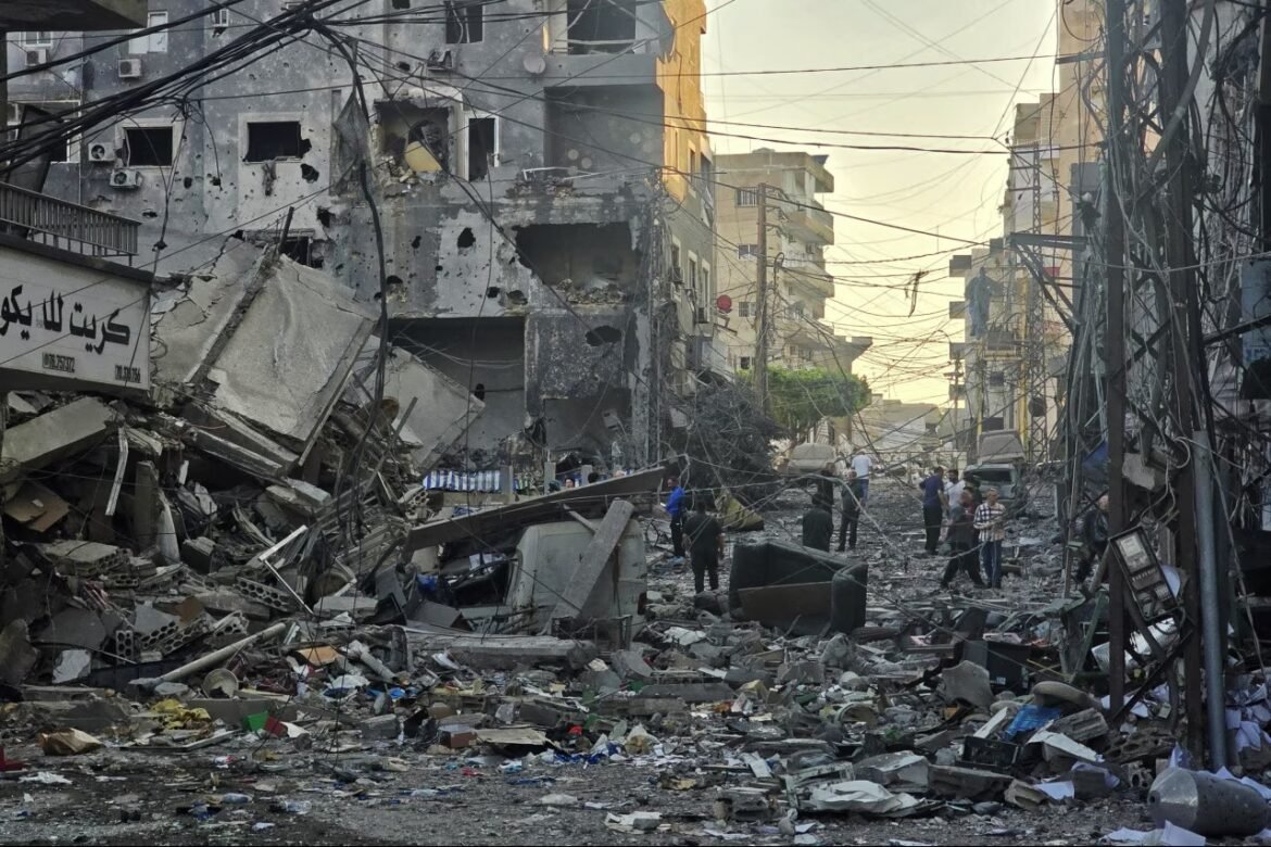 Damaged city street with collapsed buildings and tangled wires; people survey rubble in the distance.