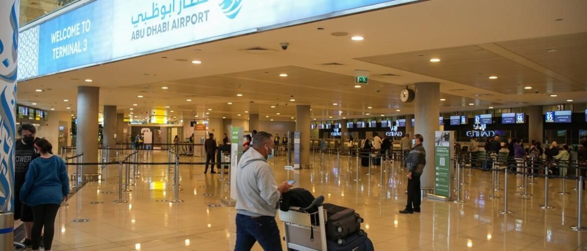 Interior of Abu Dhabi Airport Terminal 3 with a large 'Welcome to Terminal 3' sign overhead and travelers with luggage in a bright hall.