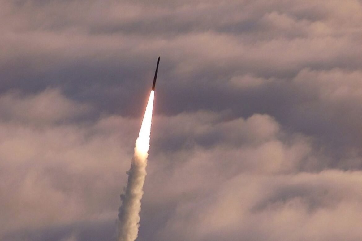 Rocket launches upward through a cloudy sky, leaving a bright flame and white exhaust plume behind it.