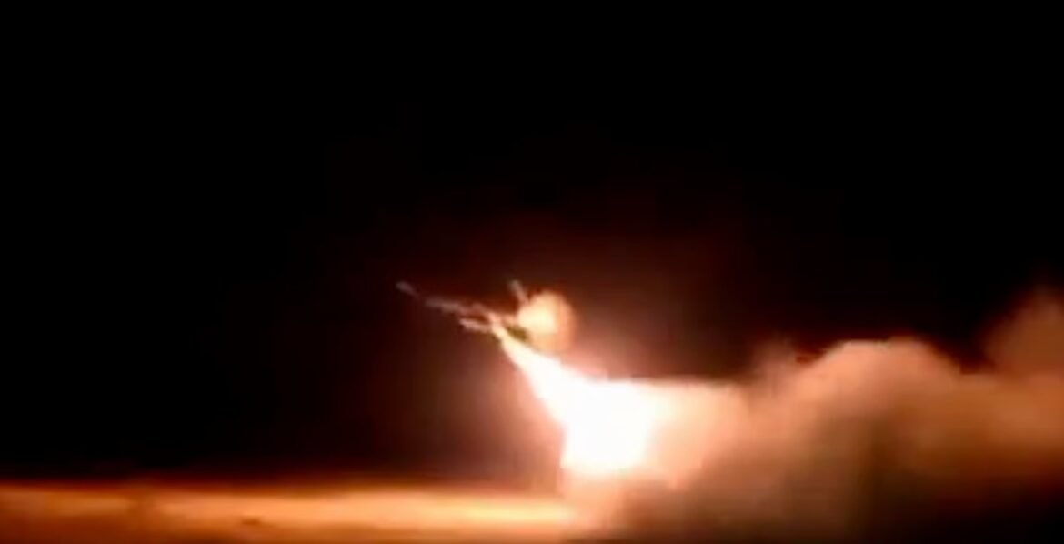 Nighttime rocket launch with a bright orange flame and smoke trail rising from the ground behind the blazing plume.