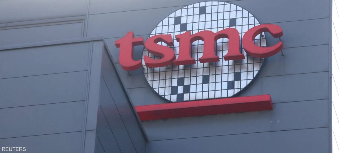 Red lowercase 'tsmc' logo on a gray wall with a black-and-white checkered circular background.