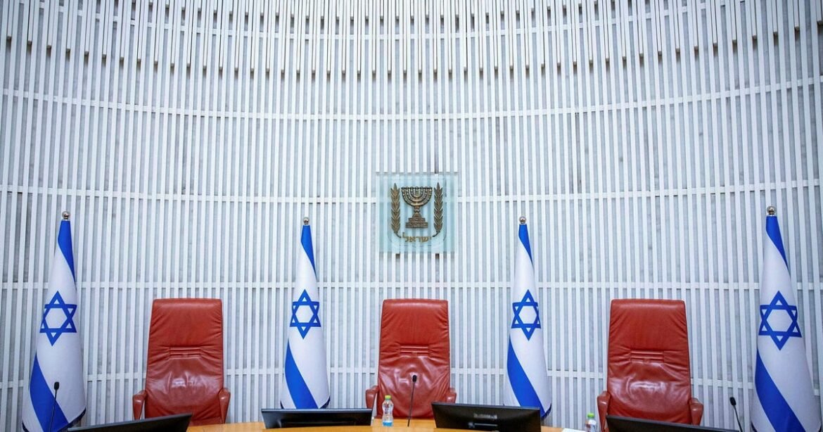 Empty Israeli government conference room with four red chairs, flags, and a crest on the wall behind a panel table