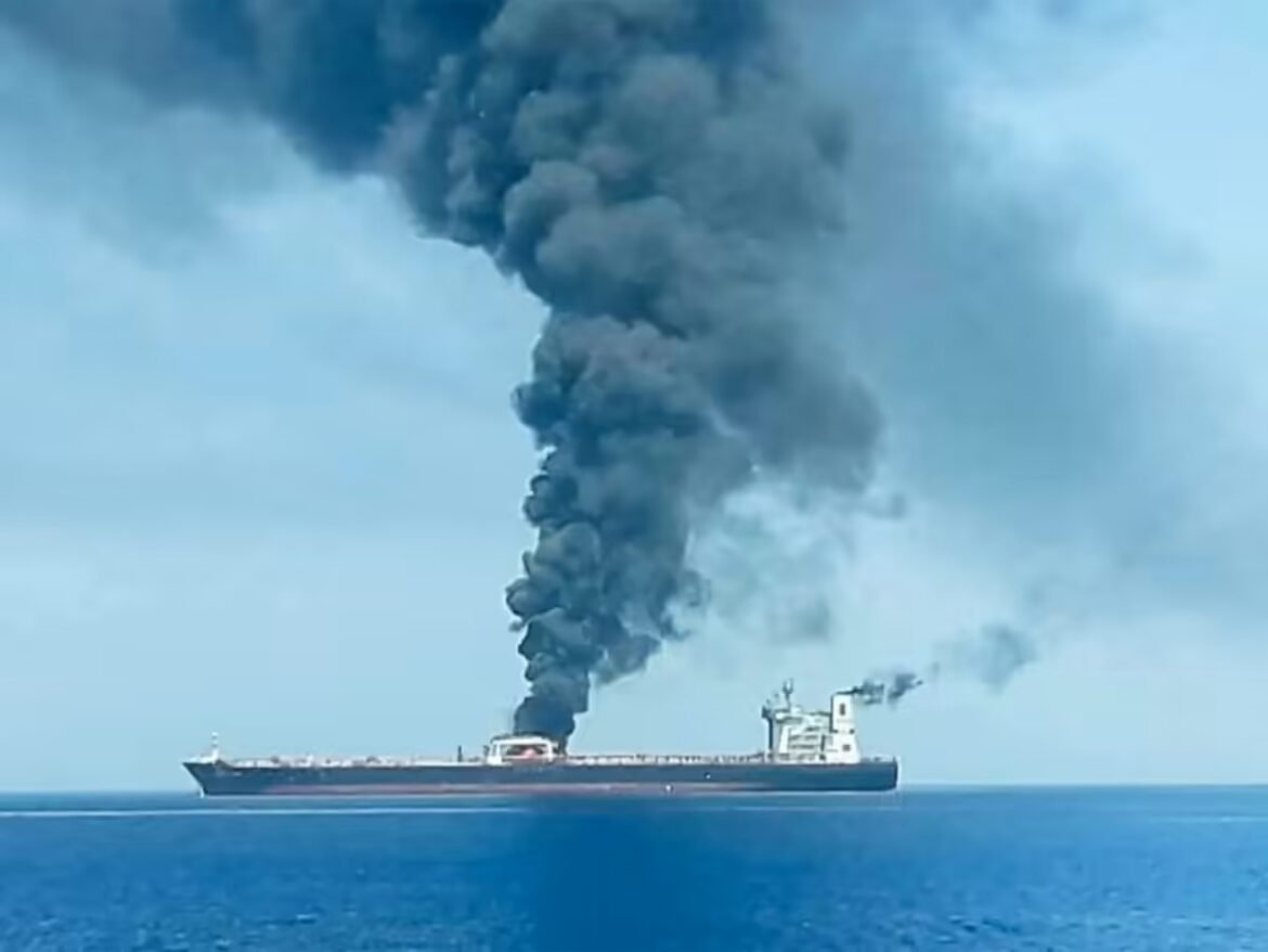 Cargo ship on calm blue water emitting a tall plume of thick black smoke from its smokestack.