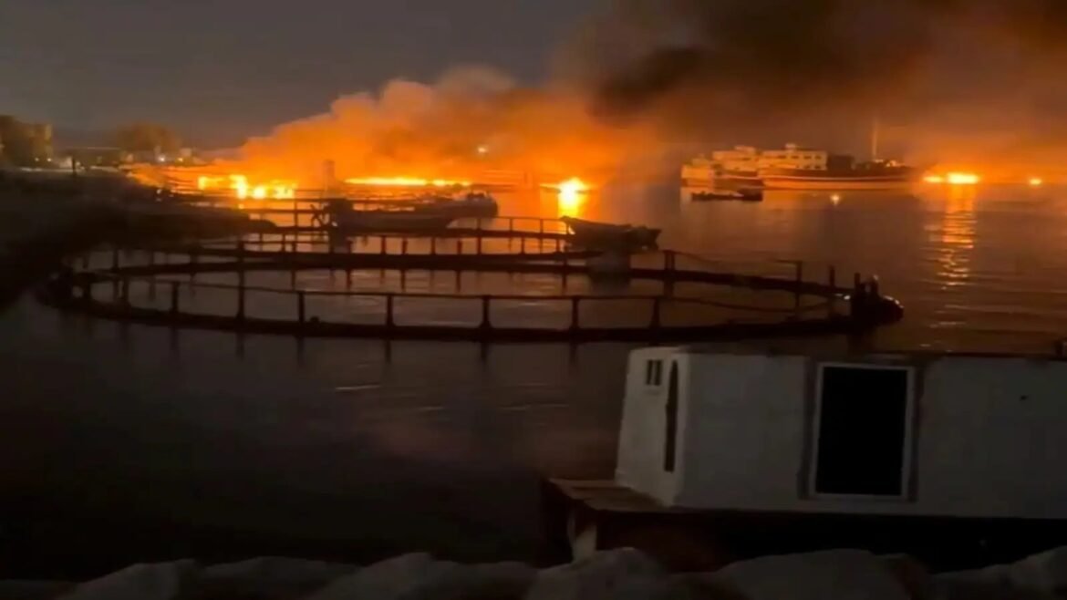 Nighttime harbor fire: boats and piers ablaze with bright flames and thick smoke reflecting on the water.