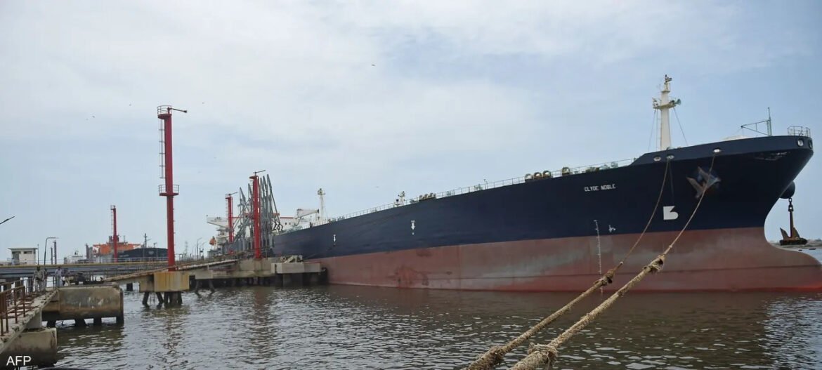 Large dark blue cargo ship named Clyde Noble moored at a port, with a red hull section below waterline and cranes in the background.