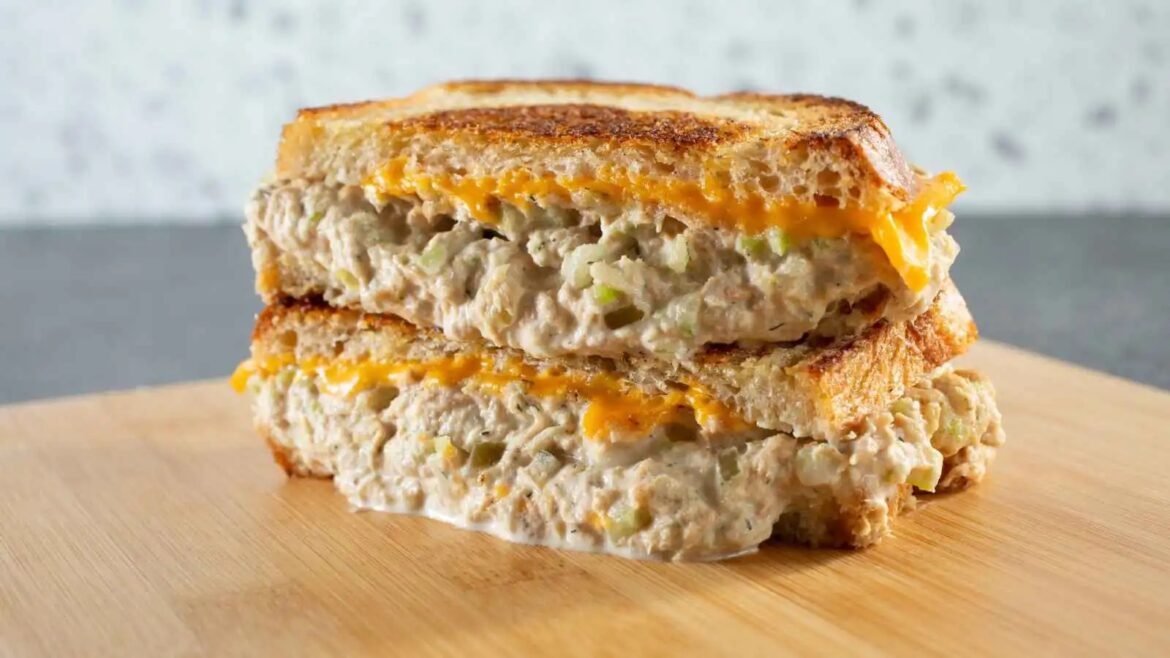 Two slices of grilled bread with creamy tuna salad and melted cheddar, stacked on a wooden board.
