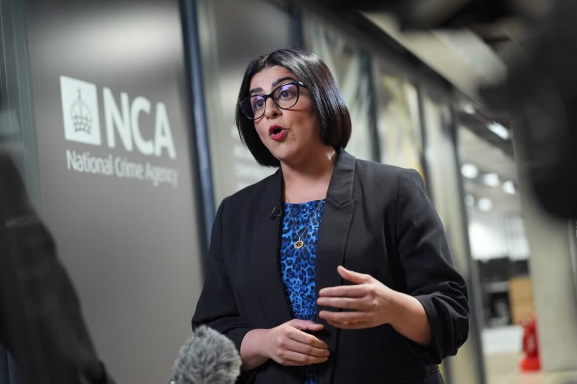 Woman in a black blazer speaks during an interview outside an NCA (National Crime Agency) facility, microphone in frame.