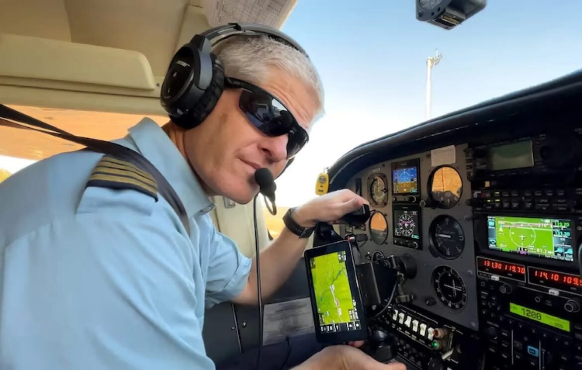 Pilot wearing headset and sunglasses in small aircraft cockpit, holding a tablet with a moving map.