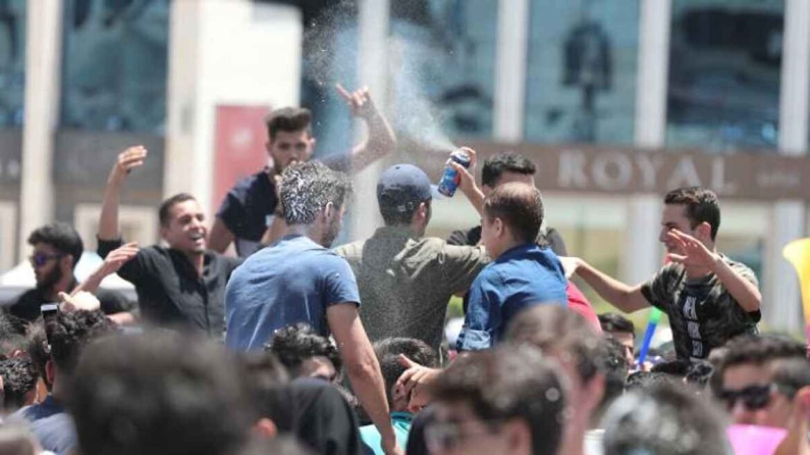 A crowded group of young people celebrating outdoors, spraying a can to create a mist over the crowd.