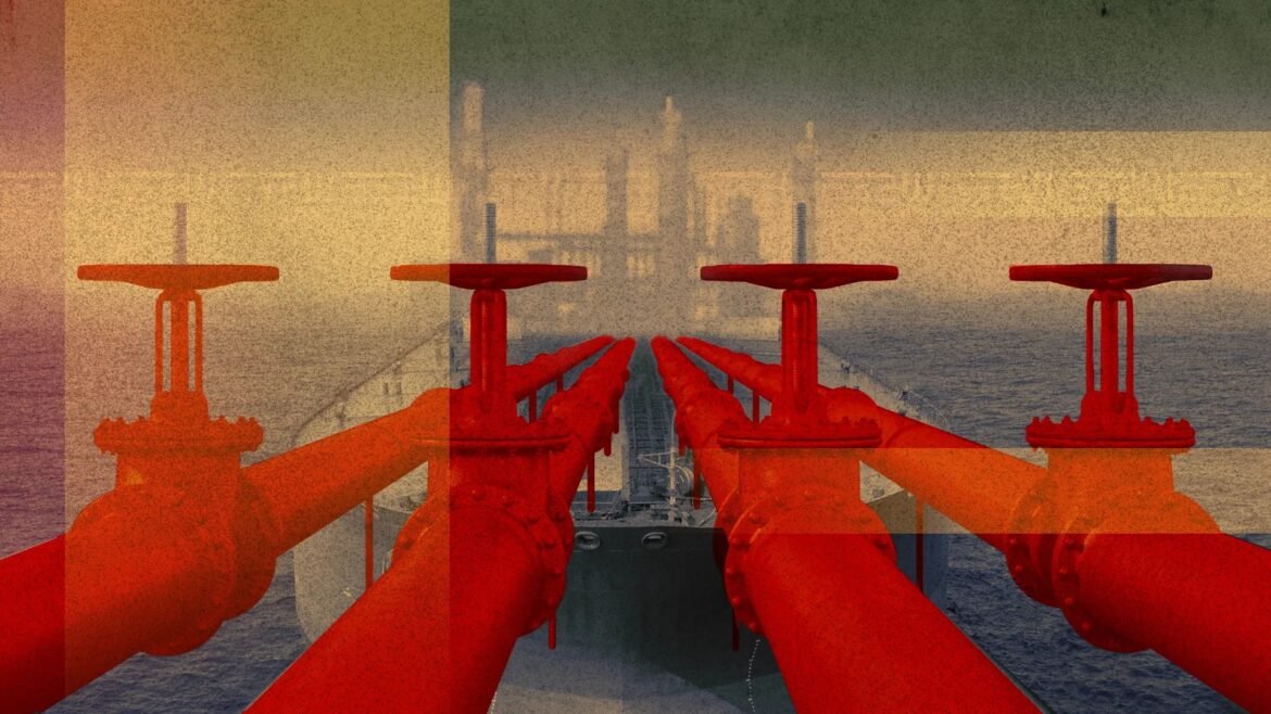 Red industrial pipes and valves run along a ship’s deck toward the horizon over the sea, with a distant skyline visible in the background.