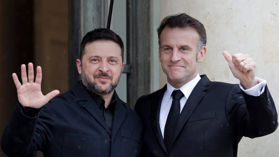Two men in black suits pose outside, smiling and waving at the camera (one with open hand, one with a raised thumb).