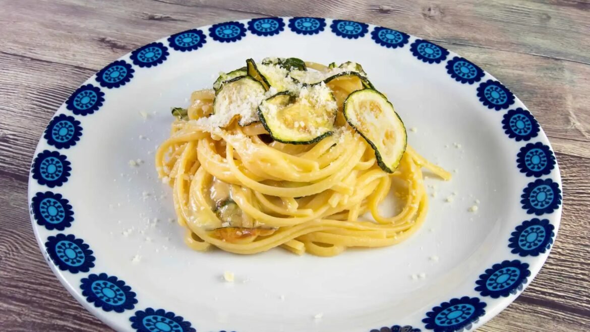 Spaghetti with zucchini chips and grated cheese on a white plate with a blue floral border, on a wooden table.
