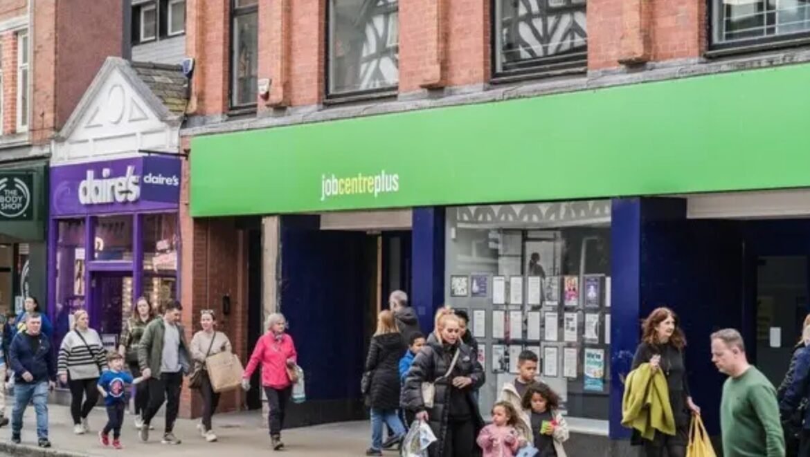 Busy street with a green Jobcentre Plus storefront and pedestrians walking by.