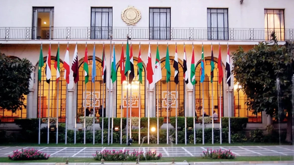 White government building with arched windows and a row of tall flagpoles displaying many international flags in front