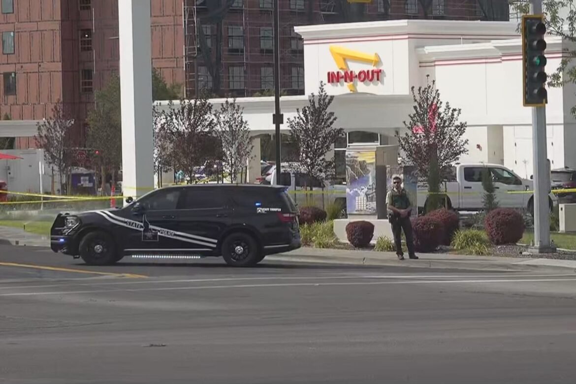 Police SUV at a storefront with yellow caution tape, an officer standing on the sidewalk outside an In-N-Out Burger.