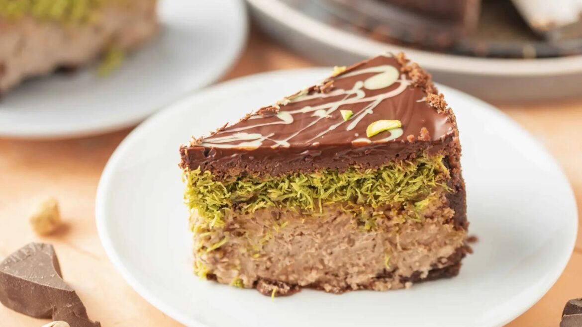 Slice of chocolate cake with pistachio filling on a white plate, topped with ganache and decorative drizzle.