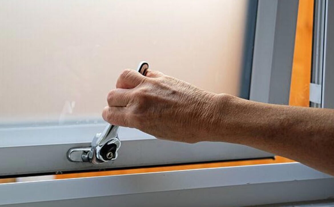 Hand gripping a lever on a gray metal control panel with an orange accent strip, close-up view.
