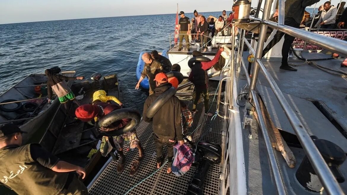 Group of people on a large boat and a small rescue dinghy in the ocean, some wearing life jackets and carrying belongings during a transfer or rescue.