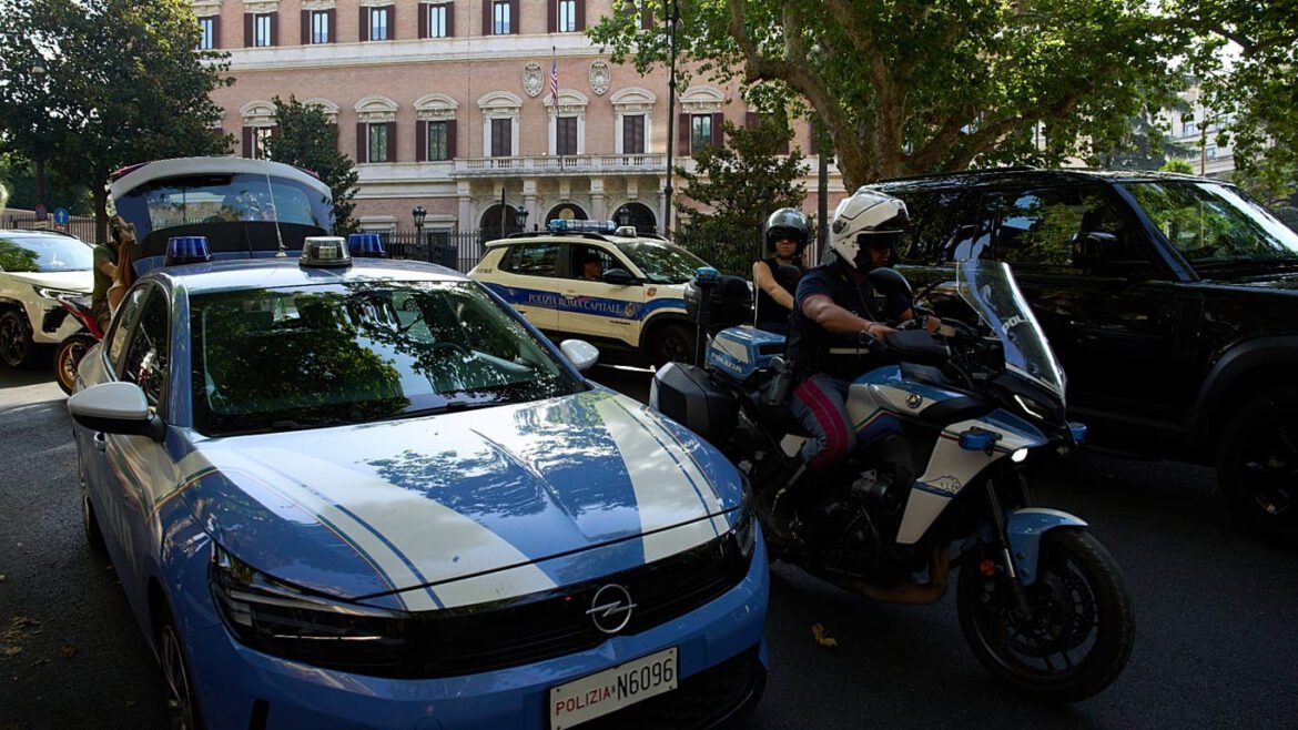 Police car and rider on a blue-and-white police motorcycle stopped on a city street with a historic building in the background.