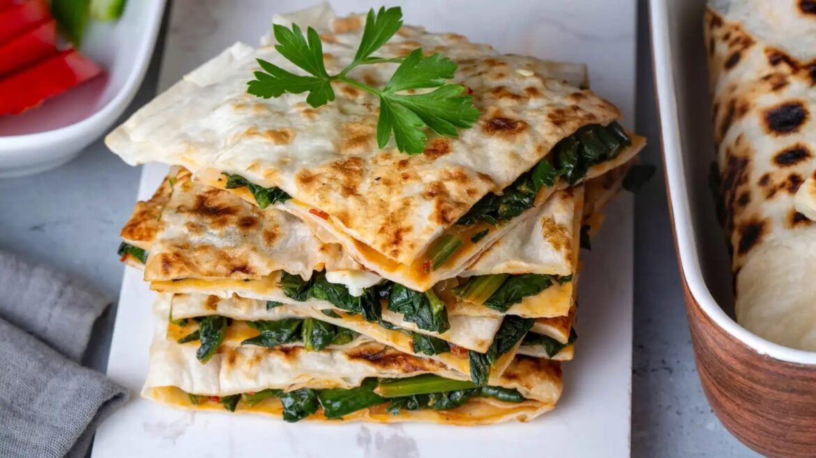 Stack of flatbreads filled with spinach and melted cheese, garnished with a parsley sprig on top.
