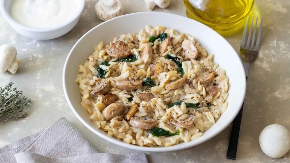Creamy chicken and mushroom pasta in a white bowl, sprinkled with pepper and greens on a light table.