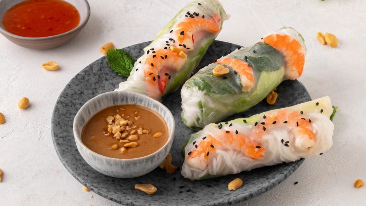 Fresh shrimp spring rolls with lettuce and rice noodles on a dark plate, served with peanut sauce on the side.