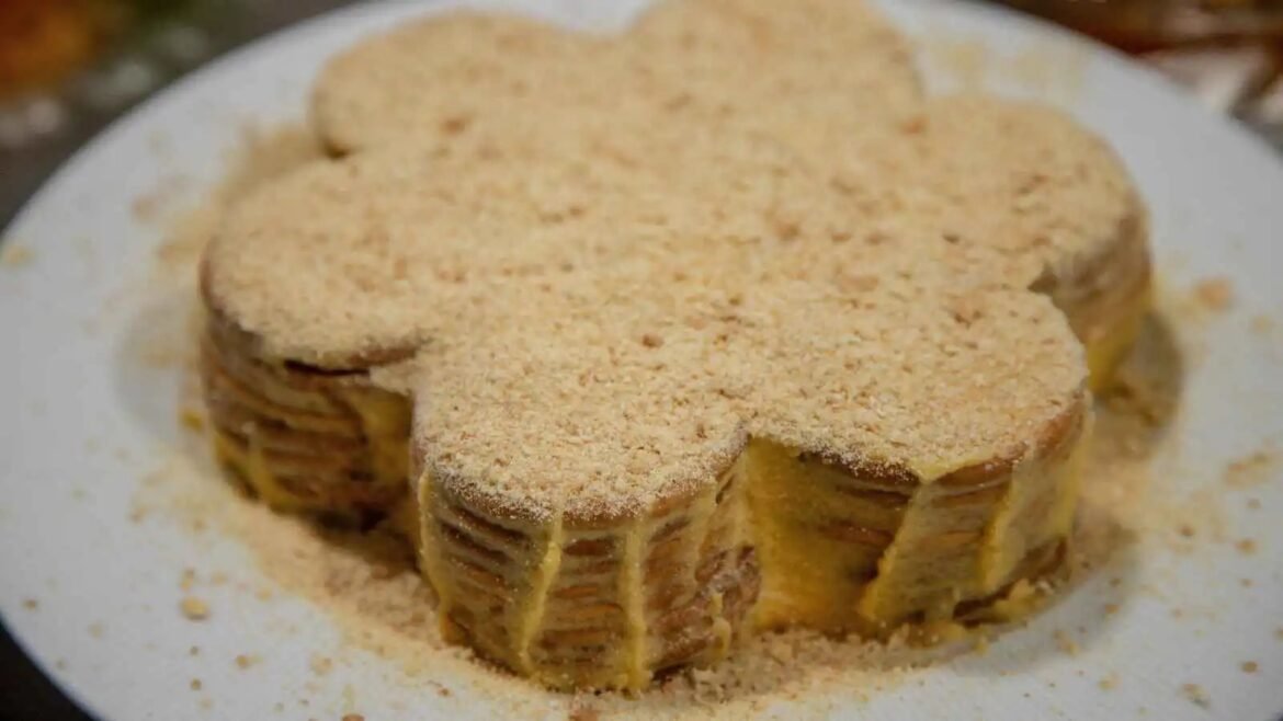Round, multi-layer cake on a white plate with a golden crumb coating and crumbs scattered around the plate.