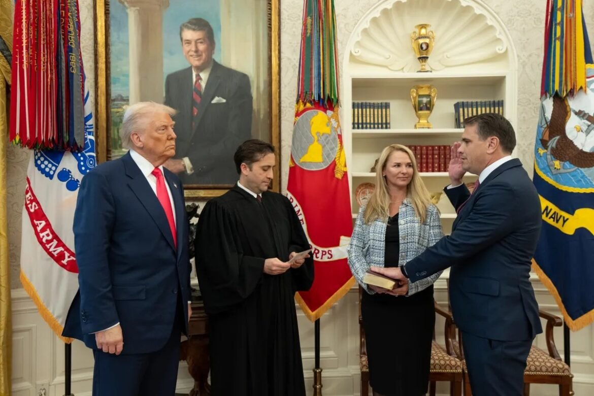 Former President Donald Trump standing in a formal room with flags, a judge in robes, and an official presenting a book to a woman in a blue blazer.