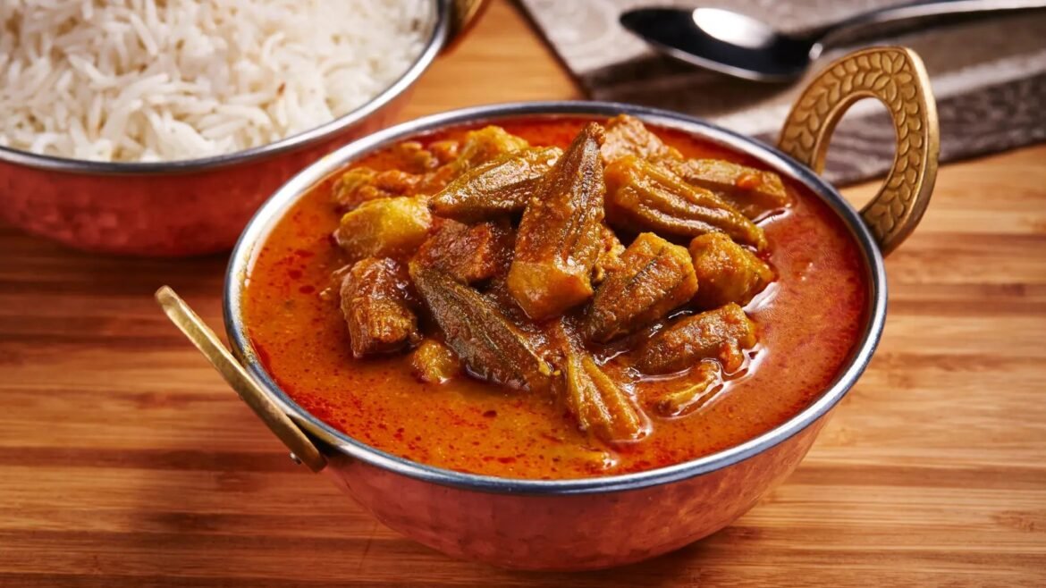 Copper bowl with spicy red curry and chunks of meat; steamed rice in the background.