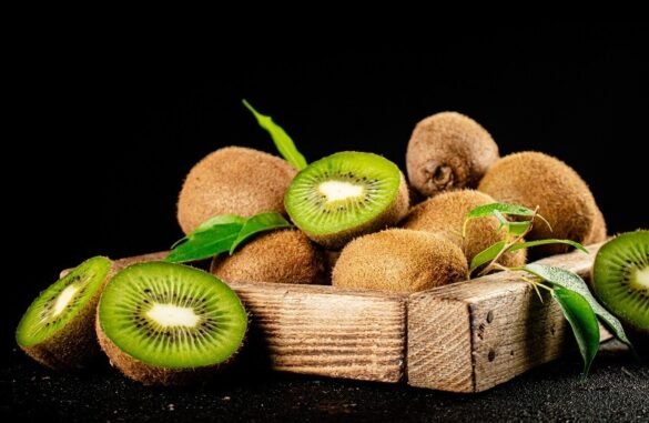 Kiwi fruits, some halved, on a rustic wooden tray against a black background.