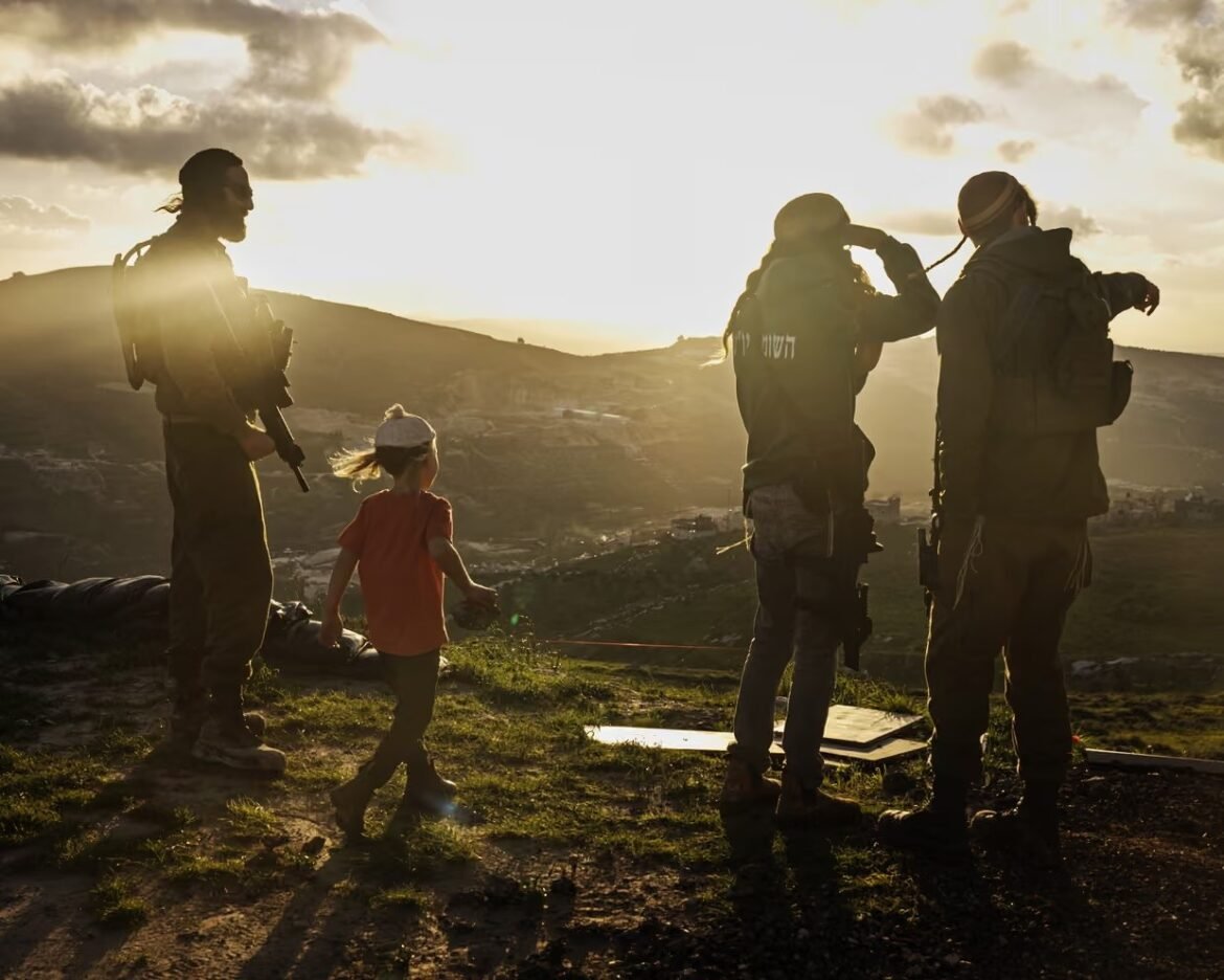 Silhouetted soldiers with backpacks on a hillside at sunset, a young child in red walks nearby as one soldier holds a rifle.